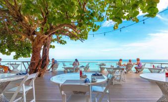 a group of people are sitting at a table on a wooden deck overlooking the ocean at Travellers Beach Resort