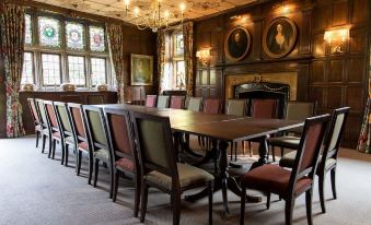 a large wooden dining table surrounded by chairs in a room with paintings on the walls at Ockenden Manor Hotel & Spa