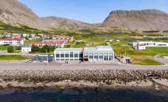a large building with a red roof is situated near the water , surrounded by mountains and grass at Fosshotel Westfjords