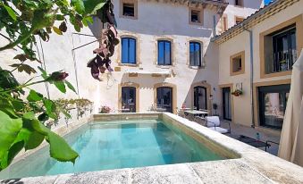 a large pool is surrounded by a brick house with a patio and potted plants at La Bastide