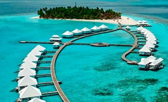 aerial view of a tropical island with multiple overwater bungalows and boats docked in the clear blue water at Diamonds Athuruga Maldives Resort & SPA