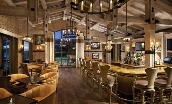 a restaurant with wooden tables and chairs , chandeliers hanging from the ceiling , and a bar area at Rancho Valencia Resort and Spa