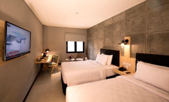 a modern hotel room with two beds , white bedding , and a desk area , under a gray wall at Ayaartta Hotel Malioboro