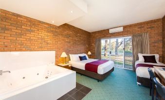 a modern hotel room with a brick wall , white bed , and bathtub , along with a window offering views of the outdoors at Thurgoona Country Club Resort