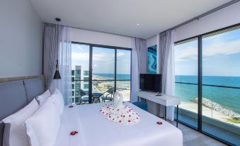 a bedroom with a large bed , white linens , and a view of the ocean through sliding glass doors at Fortune Saeng Chan Beach Hotel Rayong