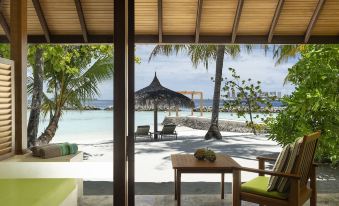 a beachfront hotel with a view of the ocean , where a wooden table and chairs are set up for dining at Kurumba Maldives