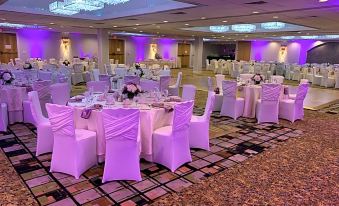 a well - decorated banquet hall with multiple tables covered in white tablecloths and adorned with flowers , creating a festive atmosphere at Holiday Inn Clinton - Bridgewater