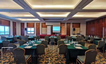 a conference room with green tables and chairs , a projector screen , and red curtains , set up for a meeting or presentation at Classic Hotel Muar