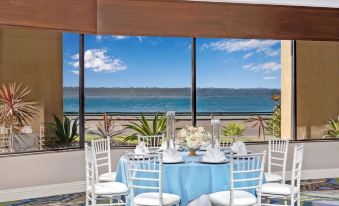a table is set with a blue tablecloth and white chairs in front of a window overlooking the ocean at Wyndham San Diego Bayside