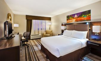 a large bed with white sheets is in a room with a chair , lamps , and a painting on the wall at Holiday Inn Washington-Dulles International Airport, an IHG Hotel