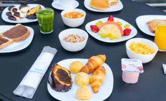 a dining table with a variety of breakfast items , including fruits , pastries , and beverages , arranged on white plates at Ibis Styles Piracicaba
