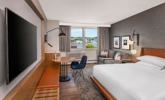 a modern hotel room with a large bed , couch , and desk , along with a view of the ocean through a window at Sheraton Portsmouth Harborside Hotel