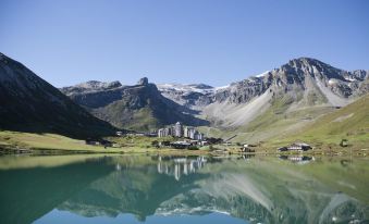 a picturesque mountainous landscape with a clear blue lake , surrounded by lush green grass and trees at Langley Hotel Tignes 2100