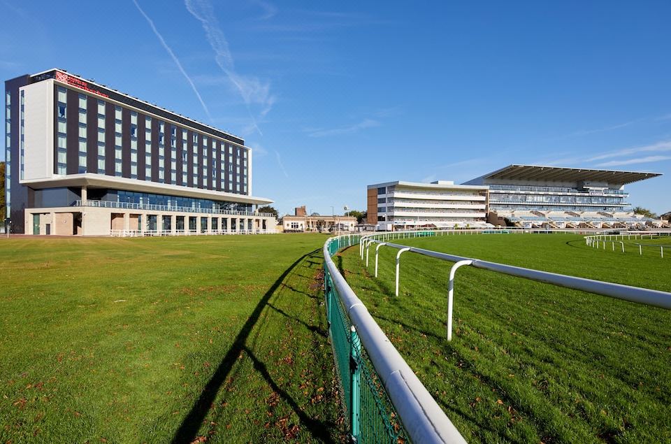 a large green grassy field with a white fence and a tall building in the background at Hilton Garden Inn Doncaster Racecourse