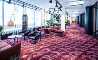 a large , well - lit room with red carpet and multiple couches arranged in various positions , creating an inviting atmosphere for meetings or gatherings at Scandic Falkoner