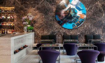 a room with purple chairs , tables , and a large abstract painting on the wall , creating an elegant and inviting atmosphere at The Jaffa, a Luxury Collection Hotel, Tel Aviv