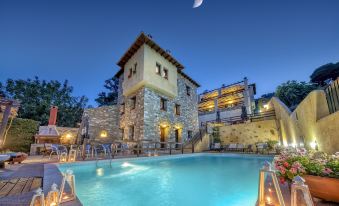 a large stone house with a pool in front of it , surrounded by trees and lit up at night at Hotel Petradi