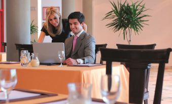 a man and a woman are sitting at a table in a restaurant , working on their laptops at Grand Mercure Petra