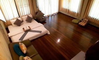 a spacious bedroom with hardwood floors , a large bed , and several pieces of furniture such as a couch and chairs at BaanSuanLeelawadee Resort Amphawa