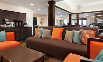 a modern living room with a brown couch , multiple pillows , and a coffee table , as well as a view of the kitchen through an open at Spring Lake Inn & Suites - Fayetteville