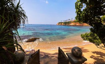 a beautiful beach with clear blue water , surrounded by lush green trees and a sandy shoreline at Eraeliya Villas & Gardens