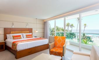 a hotel room with a king - sized bed , an orange chair , and a large window overlooking the ocean at Hotel Dann Cartagena