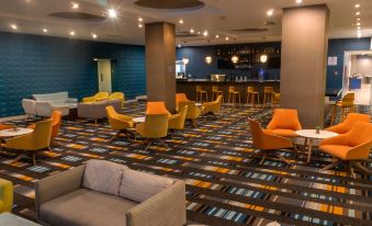 a modern lounge area with orange and yellow chairs , a bar , and blue walls , illuminated by hanging lights at Marriott Maracay Golf Resort