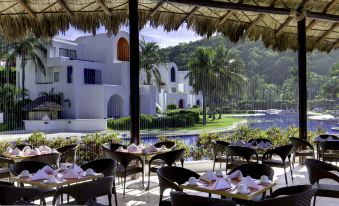 a restaurant with tables and chairs set up for guests to enjoy a meal by the pool at Camino Real Zaashila Huatulco