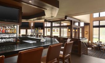 a bar with a black counter and leather chairs , featuring a tv on the wall at DoubleTree by Hilton Hartford - Bradley Airport