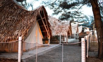 a group of thatched - roof tents are set up in a fenced - in area with trees in the background at Cabana Retreat - Glamping