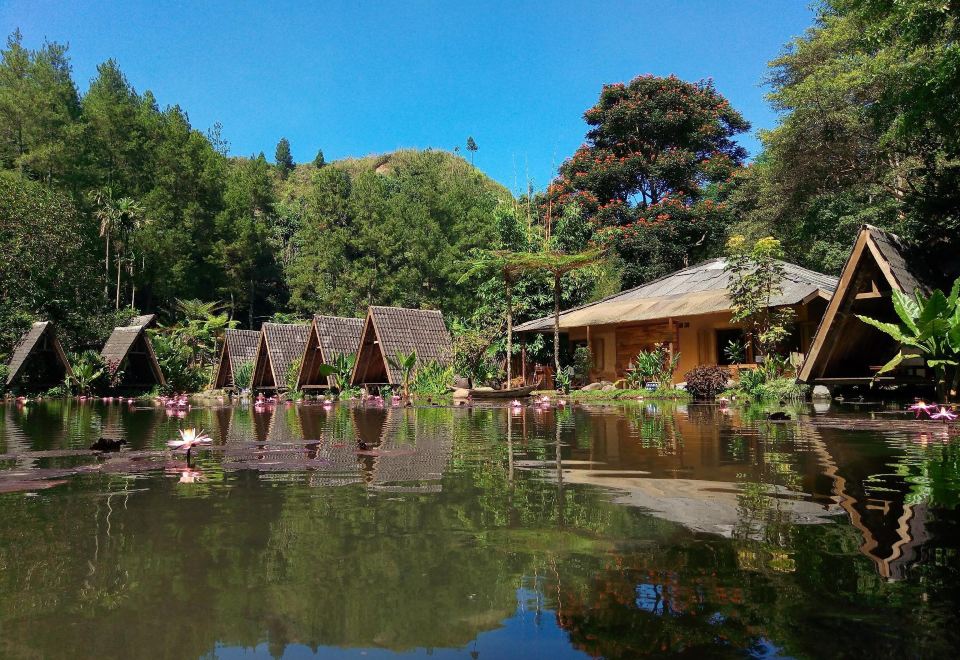 a serene lake surrounded by lush greenery , with a group of wooden cabins lining the water 's edge at Imah Seniman
