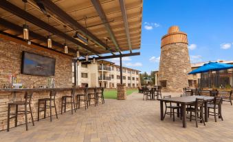 a patio area with a large brick building in the background , and several tables and chairs set up for outdoor dining at Squire Resort at The Grand Canyon, BW Signature Collection