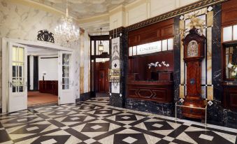 a grand hotel lobby with black and white checkered flooring , a check - in desk , and elegant furniture at Hotel Bristol, a Luxury Collection Hotel, Vienna