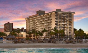 a large , modern hotel with multiple balconies and palm trees on the beach during sunset at Newport Beachside Hotel & Resort