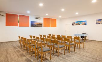 a conference room with wooden chairs arranged in rows and an orange wall adorned with three large paintings at Htop Caleta Palace #HtopBliss