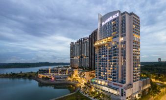 a tall , modern hotel building situated near a body of water , with the sun setting in the background at Fraser Place Puteri Harbour, Johor