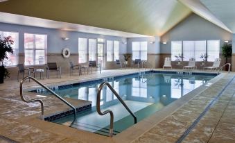 an indoor swimming pool with a diving board , surrounded by chairs and tables , in a spacious room with large windows at Residence Inn Bridgewater Branchburg