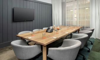 a conference room with a long wooden table , gray chairs , and a tv mounted on the wall at Canopy by Hilton Ithaca Downtown