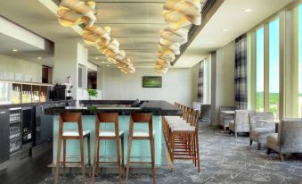 a modern bar with a green countertop , wooden stools , and hanging lights , surrounded by windows and chairs at DoubleTree by Hilton Cedar Rapids Convention Complex
