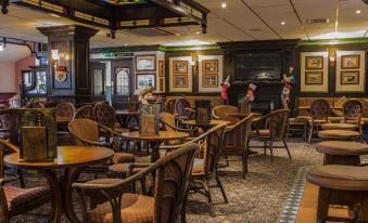 a cozy bar with wooden tables and chairs , a fireplace , and various decorations on the walls at Highfield Hotel