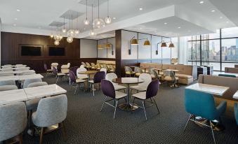 a modern restaurant with white and purple chairs , tables , and pendant lights hanging from the ceiling at Hyatt House Jersey City