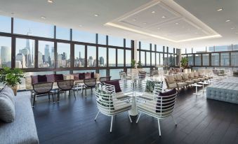 a spacious room with large windows and a dining table surrounded by chairs , overlooking a city skyline at Hyatt House Jersey City