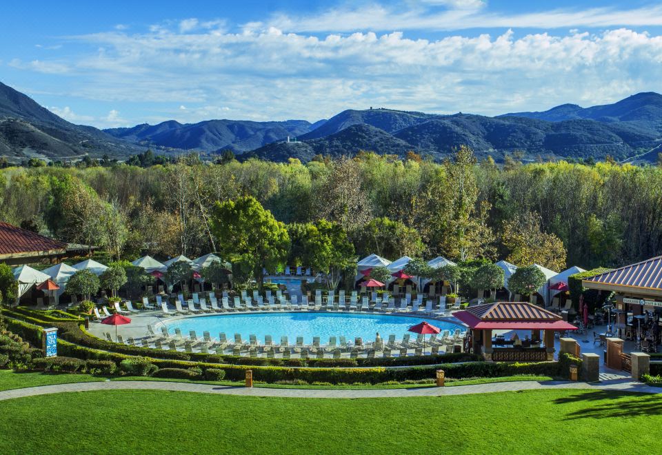 a large outdoor pool surrounded by lounge chairs and umbrellas , with a beautiful view of the mountains in the background at Pala Casino Spa and Resort