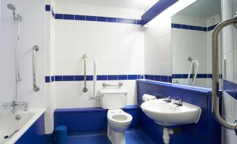 a bathroom with blue and white tiles on the walls , a toilet , sink , and mirror at Travelodge Kendal