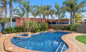 a large swimming pool surrounded by palm trees and a brick building , creating a tropical atmosphere at Peppermill Inn Motel
