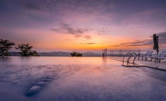 a large outdoor pool surrounded by a wooden deck , with the sun setting in the background at Coorg Cliffs Resort