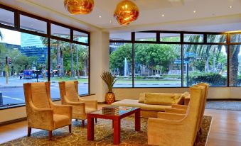 a modern lounge area with multiple chairs , a red coffee table , and large windows overlooking a city at Fountains Hotel