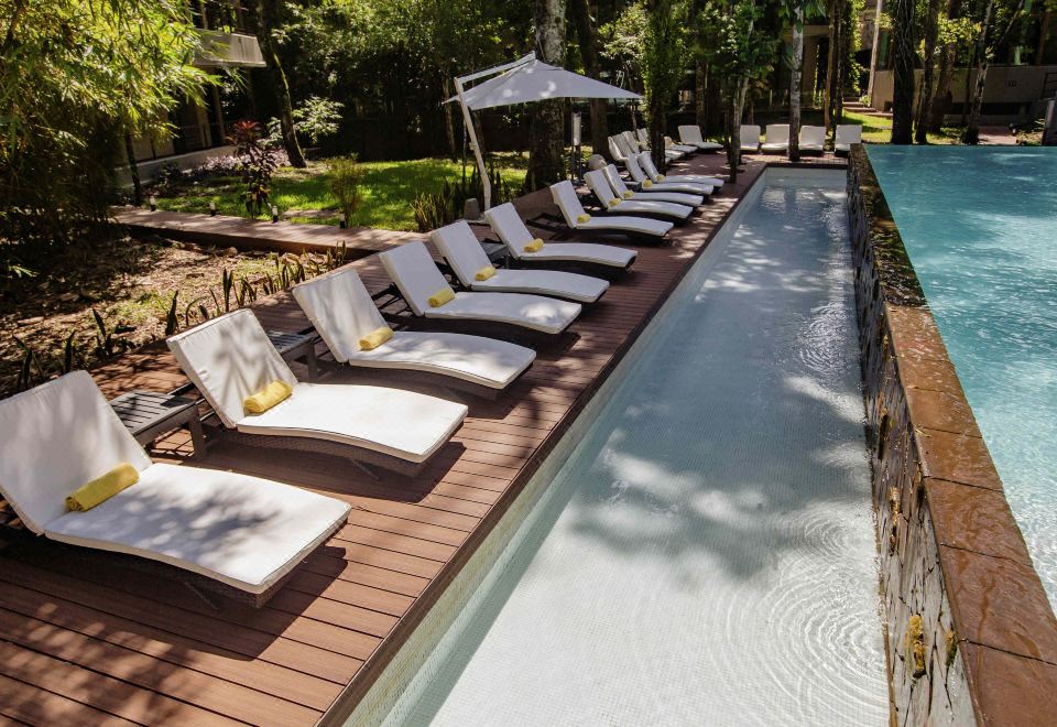 a row of white lounge chairs is lined up on a wooden deck next to a pool at Mercure Iguazu Hotel Iru