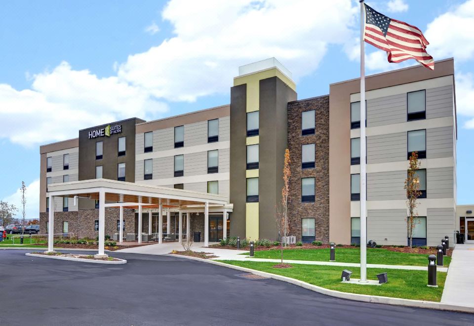 a large building with a white roof and tan walls , surrounded by grass and trees at Home2 Suites by Hilton Dickson City Scranton