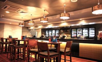 a modern bar with a wooden counter and several chairs , including one with a person sitting at one of the chairs at Rydges Mackay Suites, an EVT hotel